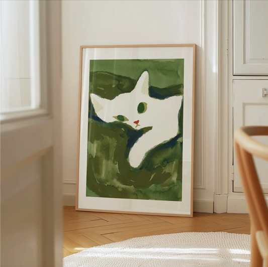 Framed artwork of a white cat on a green background in a room with wooden flooring and white walls.