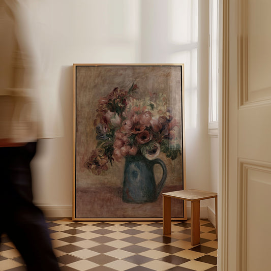 A large framed oil painting of a floral bouquet in a blue pitcher, leaning against a white wall in a room with a checkered floor and a small wooden stool.