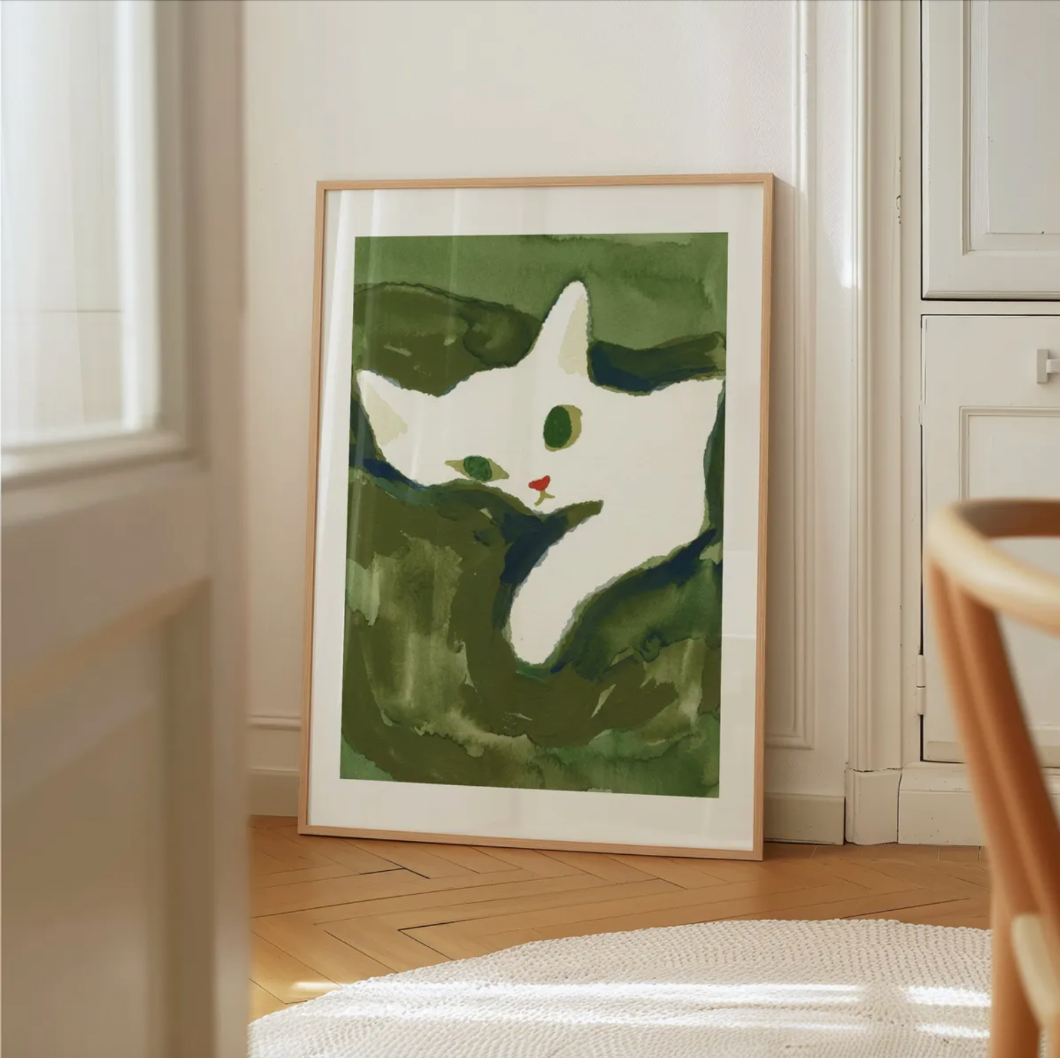 Framed artwork of a white cat on a green background in a room with wooden flooring and white walls.