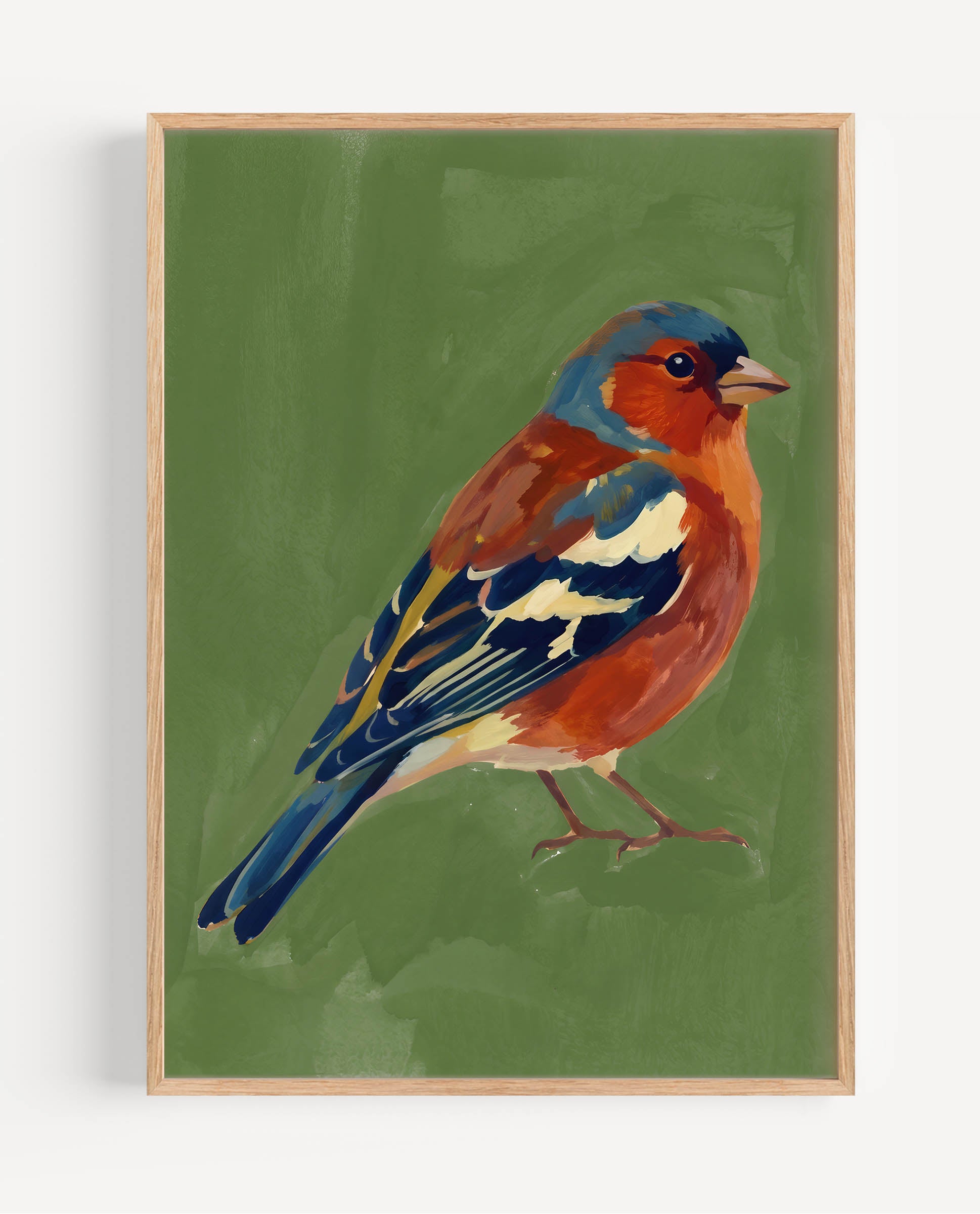 A framed painting of a chaffinch against an olive green background, featuring a light wood frame and a subtle drop shadow on a white wall.