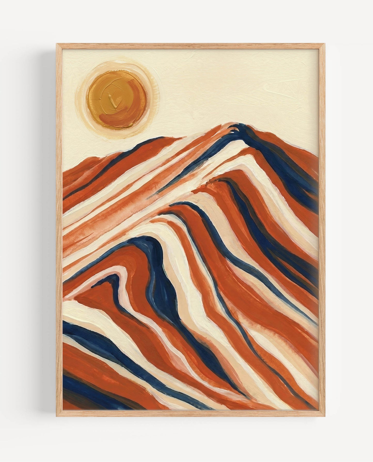 A framed abstract landscape art print featuring stylized orange and cream mountains with dark navy blue stripes and a golden sun in the upper left, set in a light natural wood frame against a white wall.