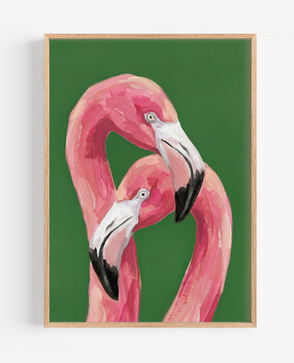 A framed art print featuring a painted pink flamingo against a solid green background, enclosed in a light natural wood frame and shown hanging on a white wall.