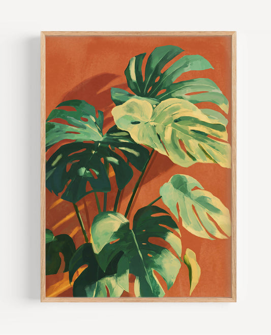 A framed botanical art print featuring green monstera leaves on a warm terracotta orange background, enclosed in a light natural wood frame and shown against a white wall.