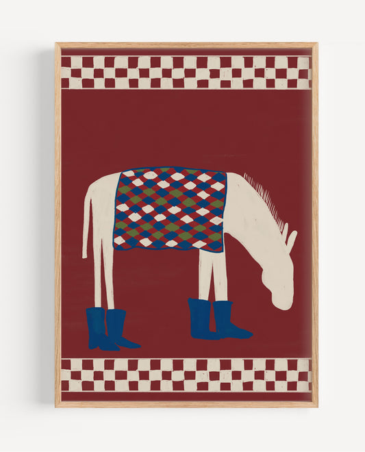 A framed art print featuring a stylized white horse wearing blue boots and a patterned blanket on a deep red background, with checkered borders at the top and bottom, housed in a light wood frame.