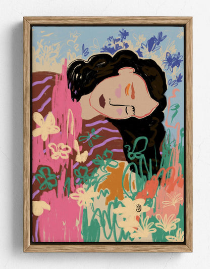A framed art print featuring a stylized illustration of a woman with dark hair surrounded by colorful flowers and abstract botanical elements, set in a light wood frame against a white wall.
