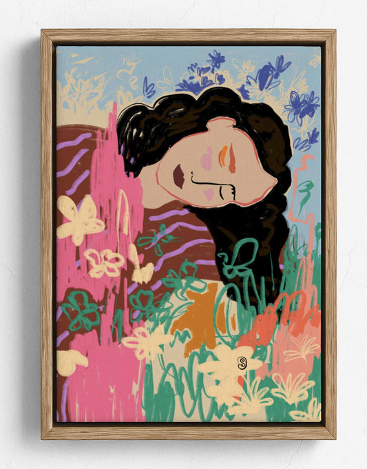 A framed art print featuring a stylized illustration of a woman with dark hair surrounded by colorful flowers and abstract botanical elements, set in a light wood frame against a white wall.