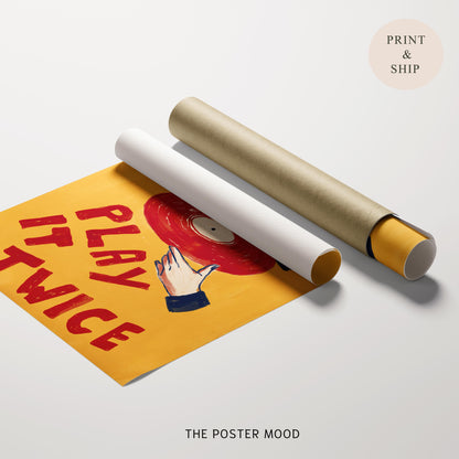 A rolled poster mockup on a light gray background, showing a partially unrolled yellow poster with red text reading 'PLAY TWICE' and a red vinyl record illustration. A second rolled section lies beside it in white and gold.