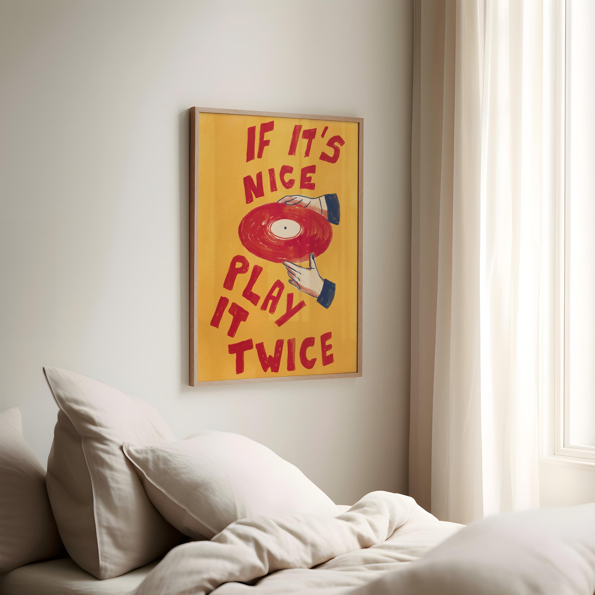 A framed wall art print with the phrase 'IF IT'S NICE PLAY IT TWICE' in red lettering over a yellow background, featuring a red vinyl record illustration, hanging above a bed in a softly lit bedroom.