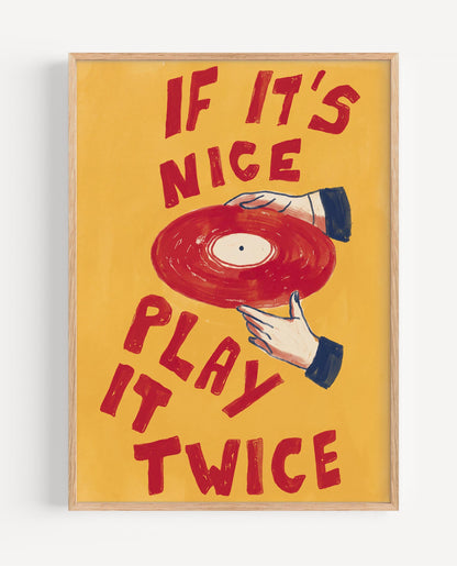 A framed art print featuring a retro illustration of a hand holding a red vinyl record against a warm yellow background, with the text 'IF IT'S NICE PLAY IT TWICE' in red. The print is housed in a light natural wood frame and is shown hanging on a white wall.