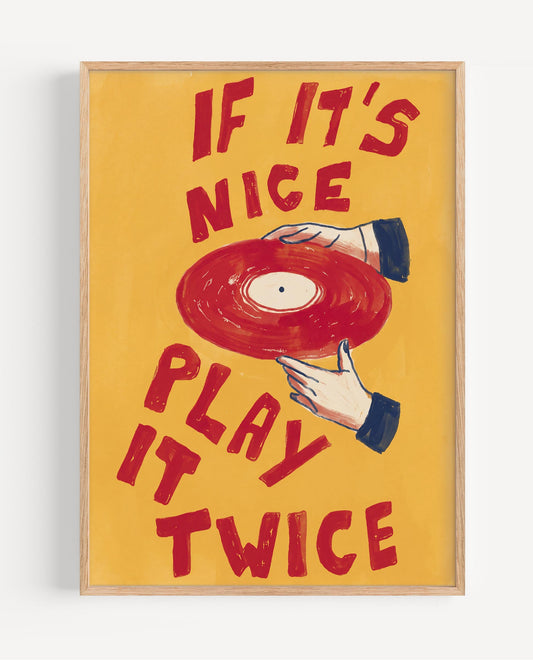 A framed art print featuring a retro illustration of a hand holding a red vinyl record against a warm yellow background, with the text 'IF IT'S NICE PLAY IT TWICE' in red. The print is housed in a light natural wood frame and is shown hanging on a white wall.