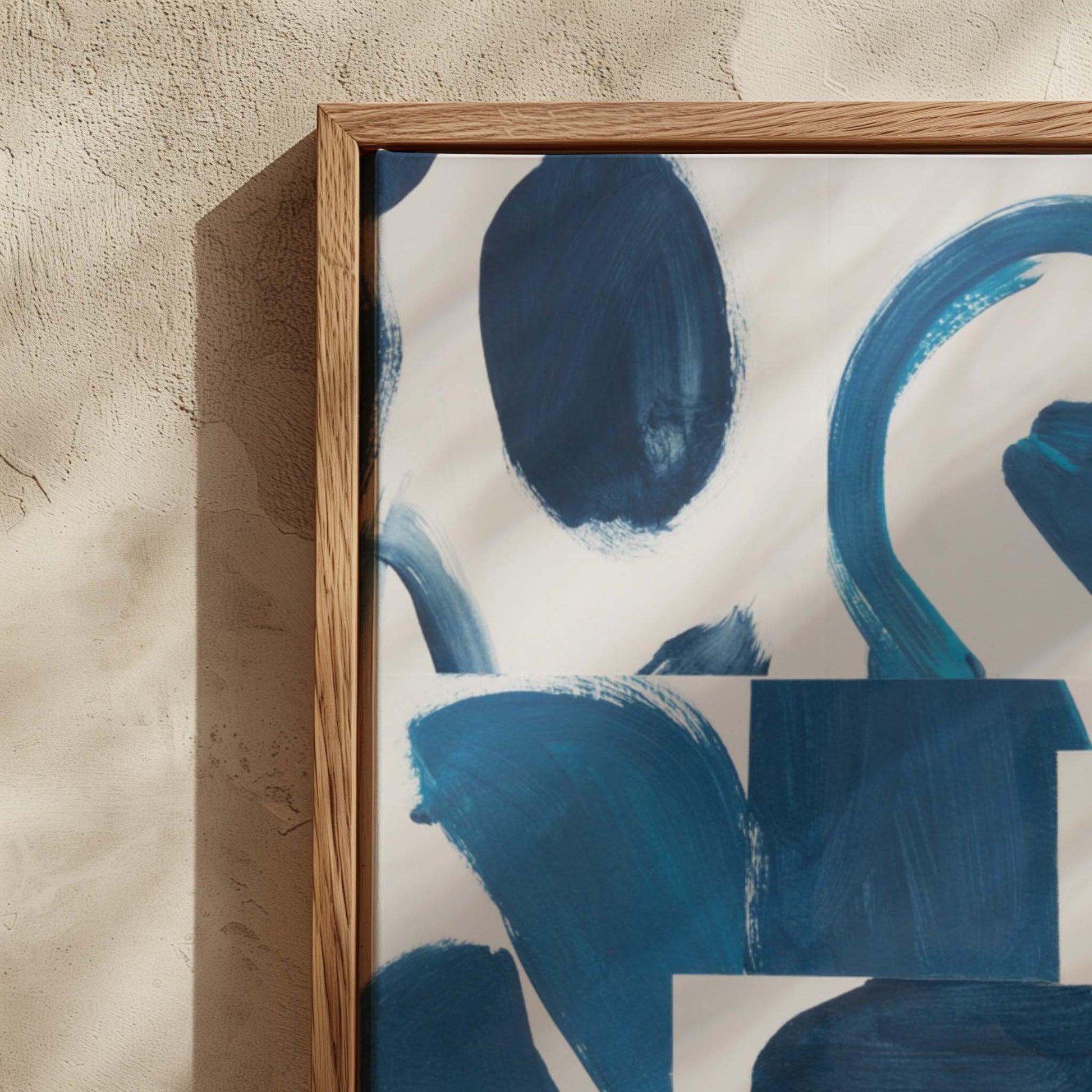 Framed abstract wall art with bold blue brushstrokes on a white background, shown in a light wood frame against a textured beige wall.