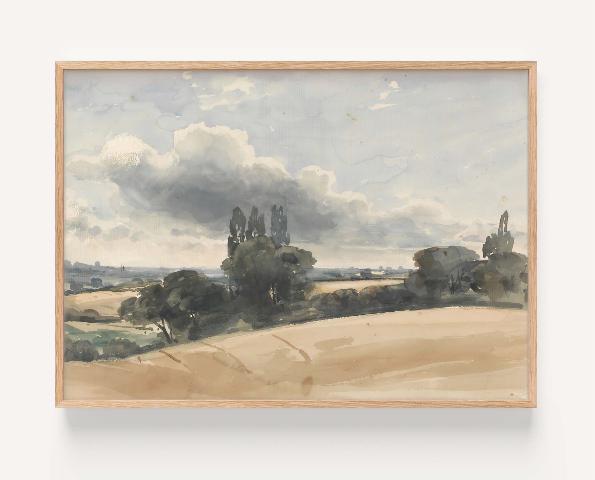 A framed landscape watercolor painting showing a muted countryside scene with fields, trees, and a cloudy sky, mounted against a light wall.