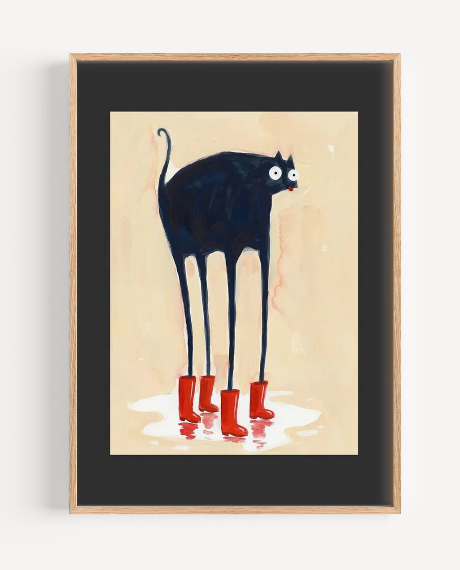 Framed wall art featuring a stylized black cat with long legs and red rain boots on a cream background, shown in a light wood frame with a black mat.