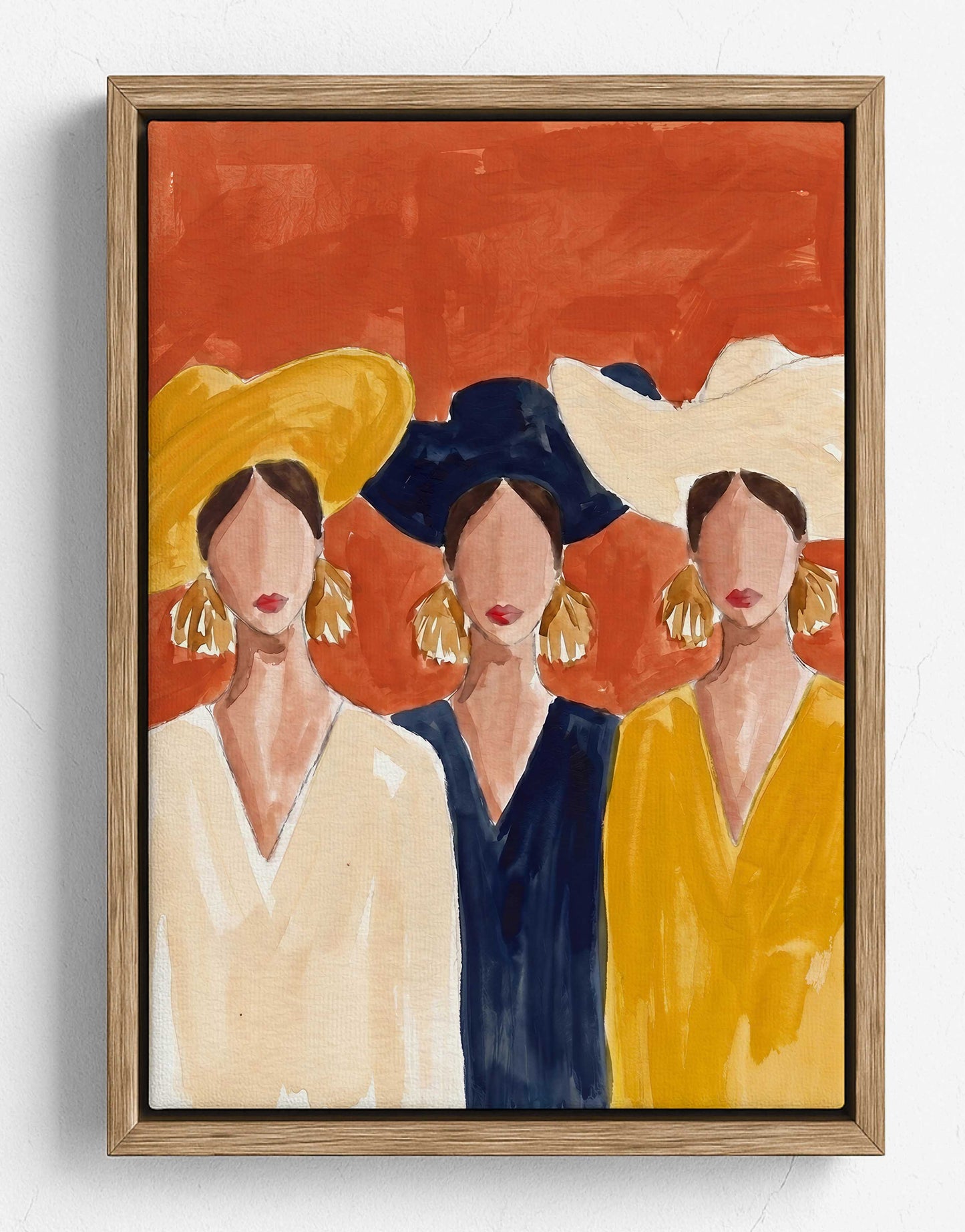 A framed painting of three stylized women wearing large hats, shown against a warm orange-red background. The artwork is housed in a light natural wood frame and hangs on a white wall.