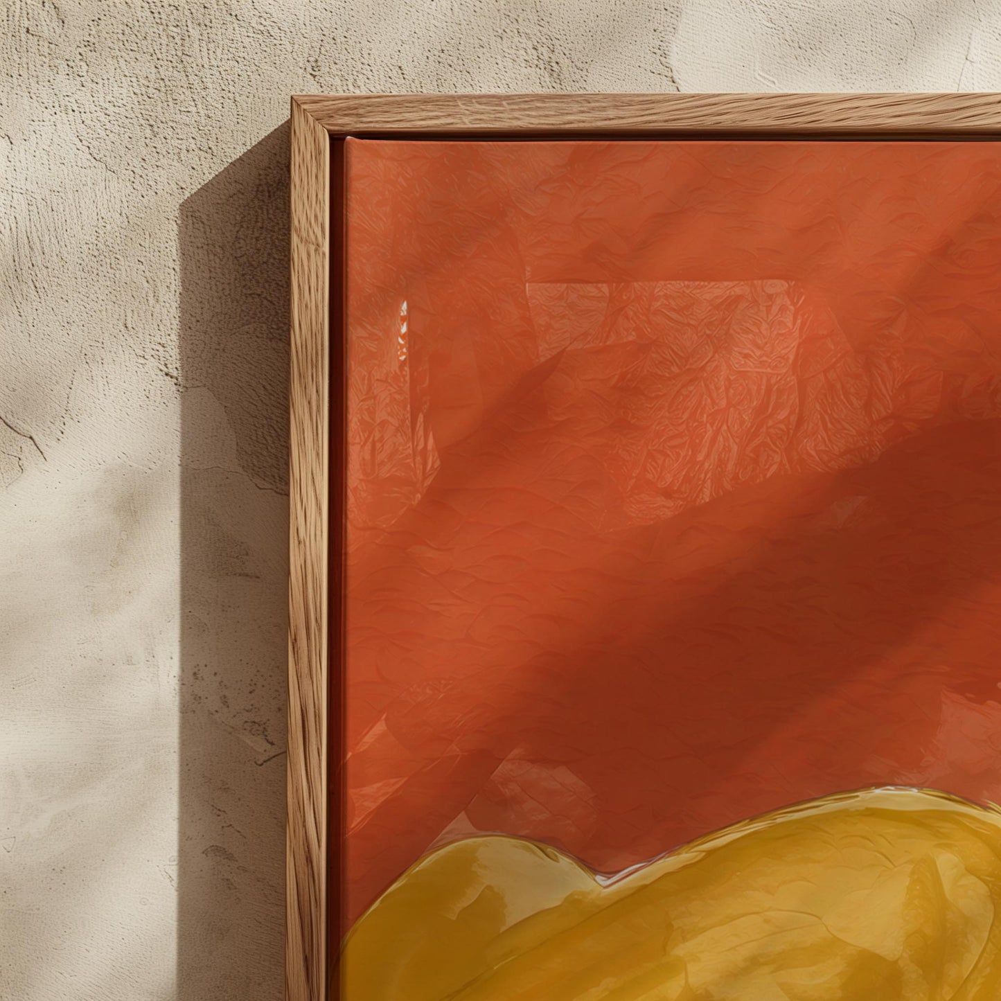A close-up of a framed abstract art print featuring a warm orange-red background with a yellow shape at the bottom and a light wood frame, mounted on a textured beige wall.