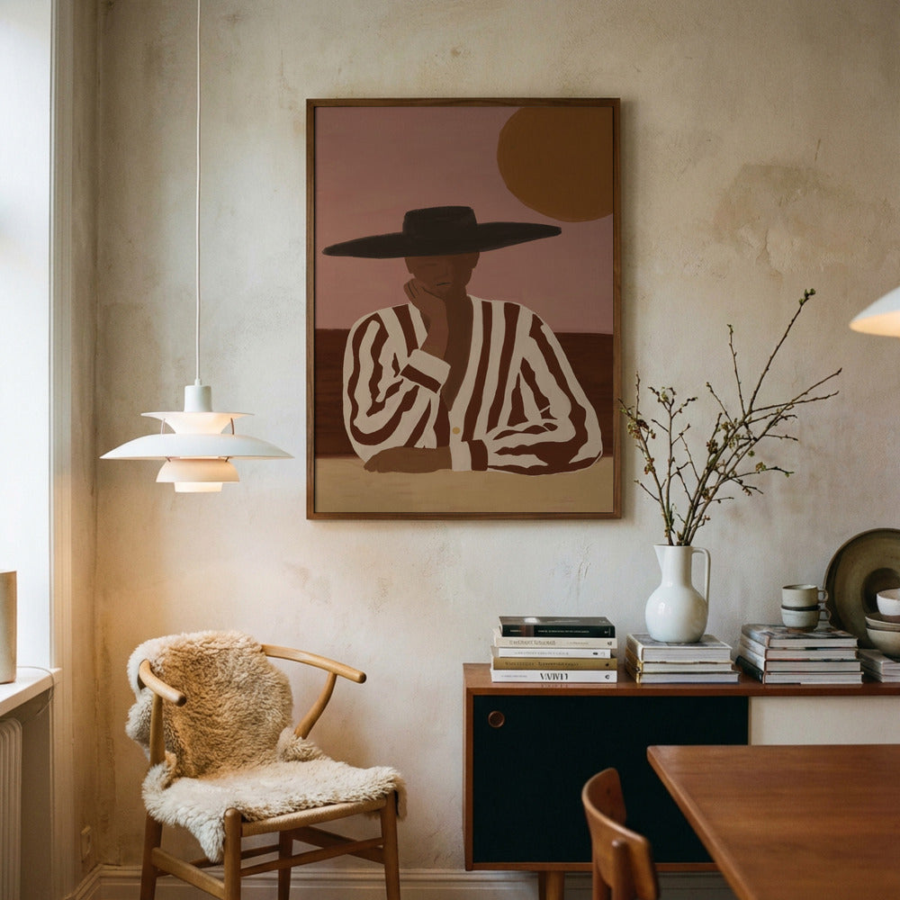 A framed art print featuring a stylized portrait of a person in a black hat and striped shirt, hanging on a textured beige wall in a warm, modern room with a wooden chair, sideboard, and vase.