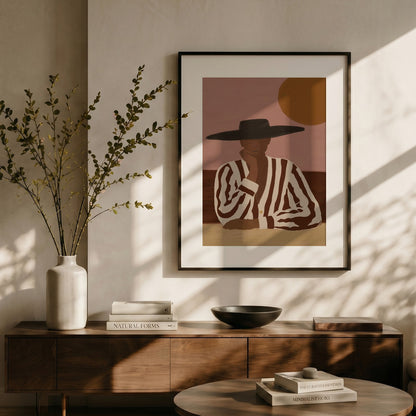 Framed artwork of a person wearing a hat on a wall above a wooden console table with decor items.
