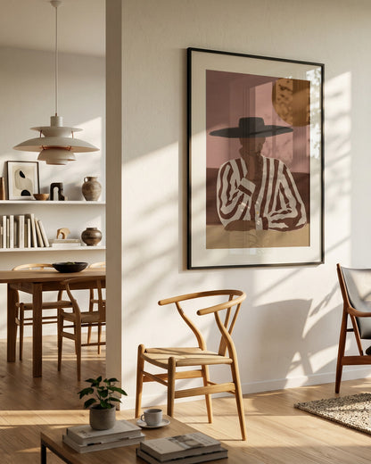 A framed art print featuring an abstract portrait of a person in a wide-brimmed hat, styled in a warm, modern living space with wooden furniture and natural light.