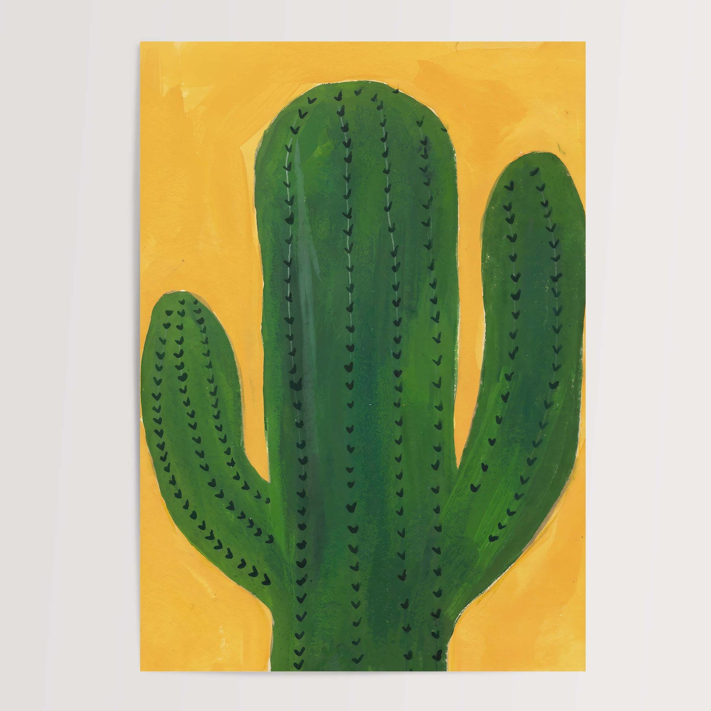A minimalist painting of a green saguaro cactus on a textured yellow background, presented as an art print against a light gray wall.