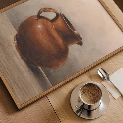 A framed still life painting of a brown ceramic pitcher on a light wood tabletop, styled with a cup of coffee, a spoon, and a napkin.