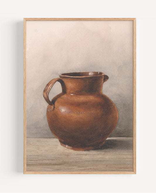 A framed still life art print depicting a brown ceramic pitcher on a tabletop against a neutral gray background, enclosed in a light wood frame.