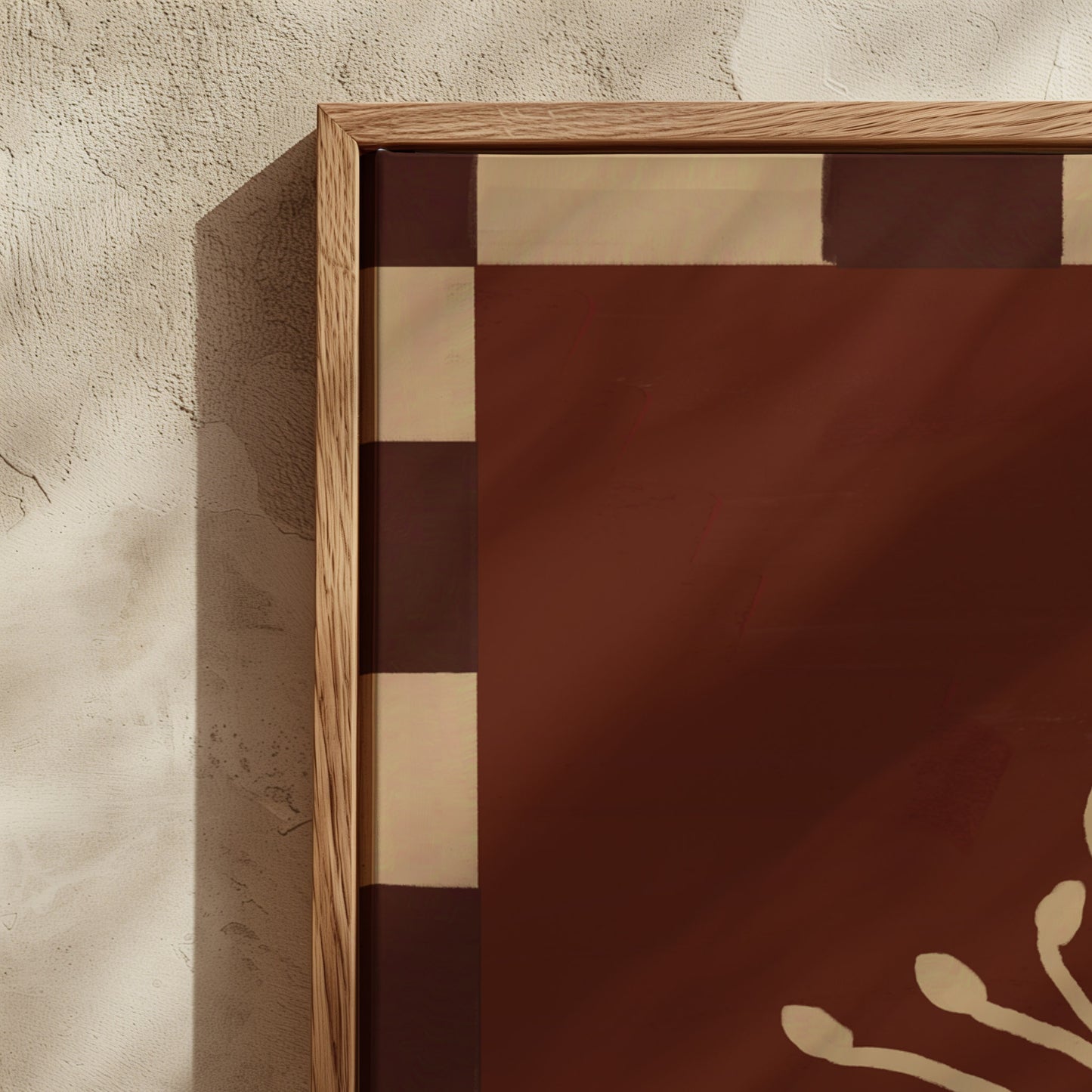 A close-up of a framed art print or panel with a warm brown and beige geometric pattern, set against a textured beige plaster wall.