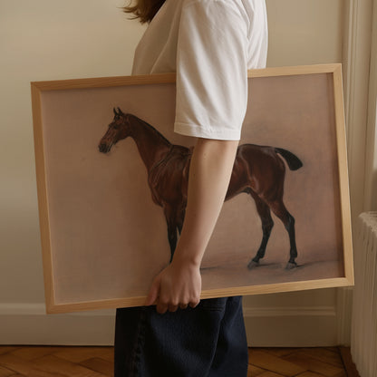 A person in a white t-shirt and dark jeans holds a large framed painting of a brown horse against a beige wall.