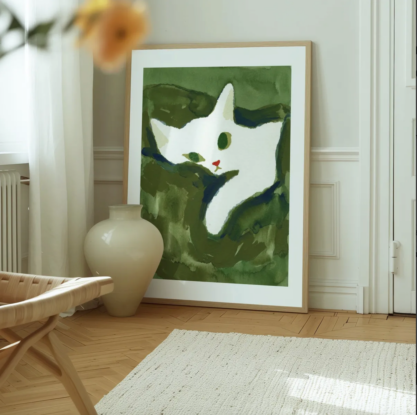 Framed artwork of a white cat on a green background in a room with a vase and chair.