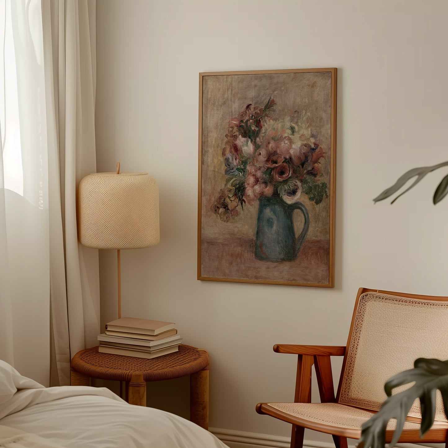 A framed floral still life painting hangs on a beige wall in a softly styled bedroom or living space, with a bedside lamp, stacked books, a woven chair, and a bed visible around it.