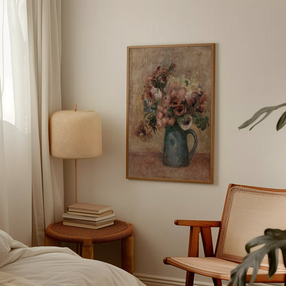 A framed floral still life painting hangs on a beige wall in a softly styled bedroom or living space, with a bedside lamp, stacked books, a woven chair, and a bed visible around it.