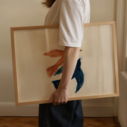 A person in a white t-shirt and dark skirt holds a large framed abstract painting featuring blue and orange brushstrokes on a cream background with a light wood frame.