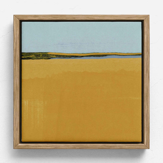 A square framed landscape painting featuring a wide mustard-yellow foreground, a distant strip of green and blue land, and a pale blue sky, set in a light natural wood frame against a white wall.